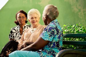 Active retired elderly women and free time, group of happy senior african american and caucasian female friends talking and sitting on bench in park